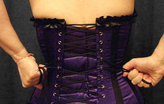 Hands pulling laces on the back of a corset tight
